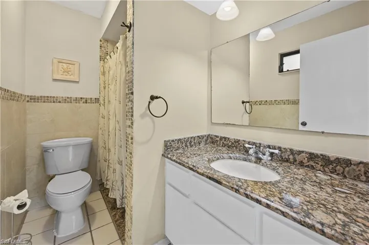 Bathroom with tile walls, toilet, vanity, and tile patterned flooring