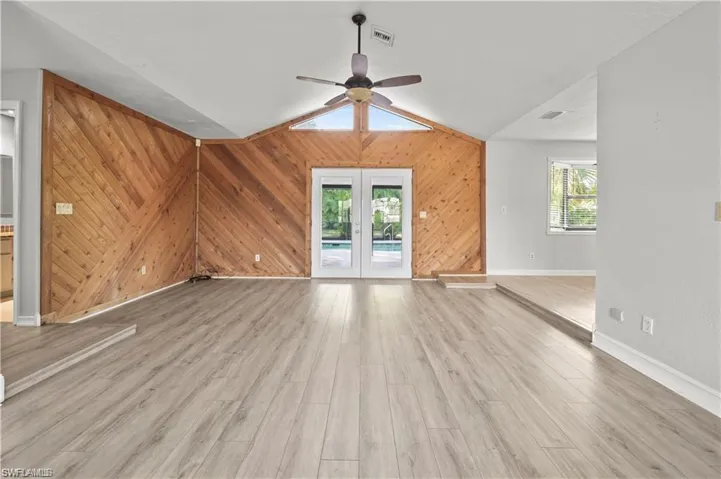 Unfurnished living room featuring wooden walls, lofted ceiling, light hardwood / wood-style floors, and a healthy amount of sunlight