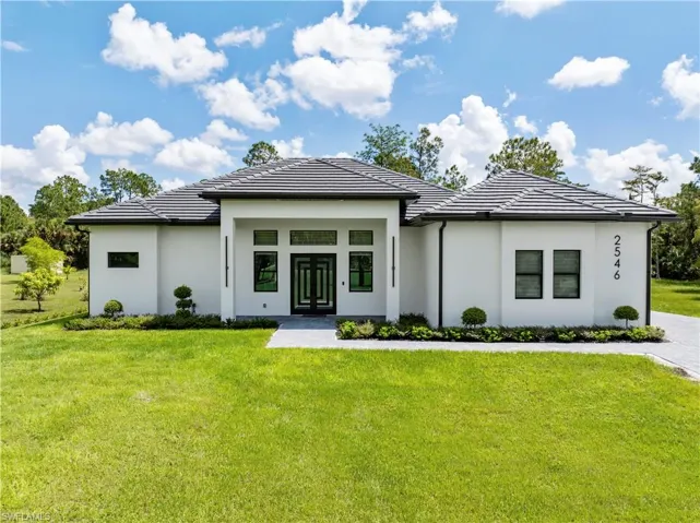 View of front of home with stucco siding, a tile roof, a front lawn, and french doors