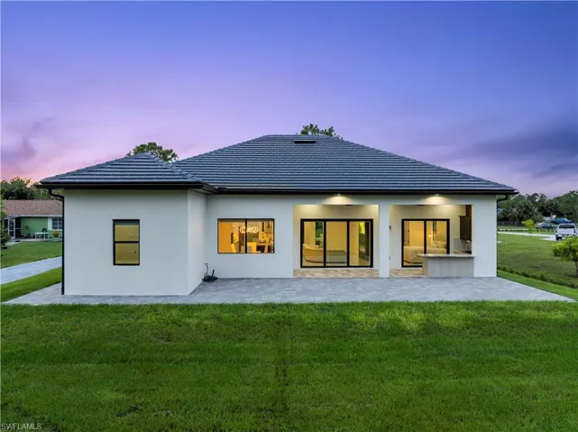 Back of house featuring a patio area, a lawn, stucco siding, and a tiled roof