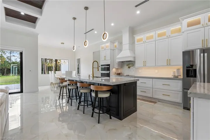 Kitchen with marble finish floor, premium range hood, an island with sink, stainless steel refrigerator with ice dispenser, and backsplash