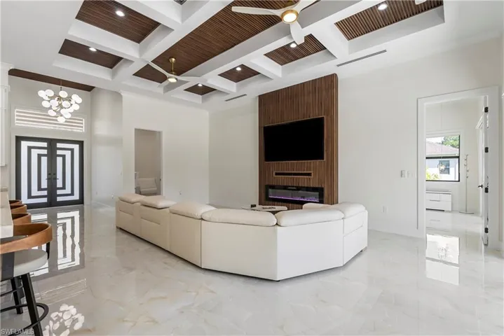 Living room with marble finish floor, a towering ceiling, ceiling fan with notable chandelier, and coffered ceiling