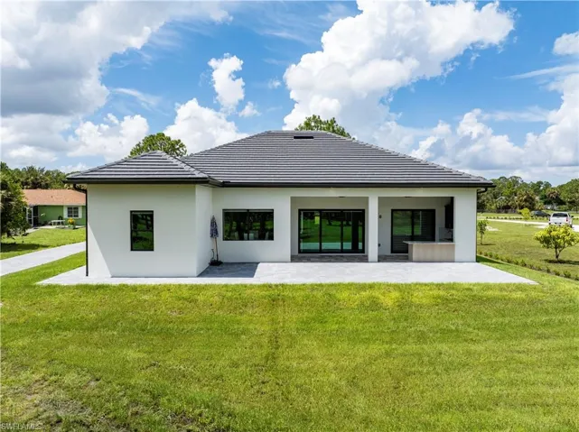 Back of property with a lawn, a tile roof, stucco siding, and a patio area