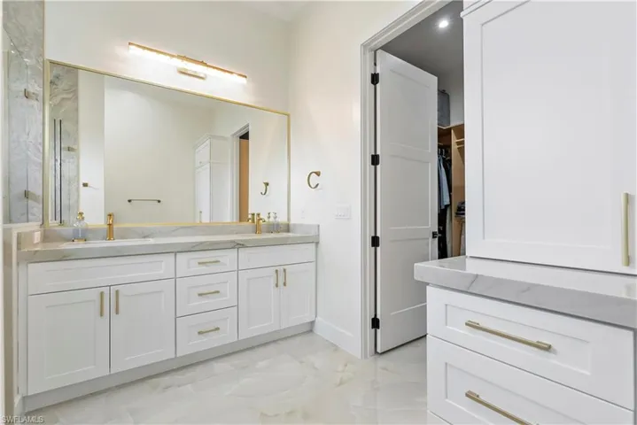 Full bathroom featuring marble finish floor, double vanity, a marble finish shower, a sink, and a walk in closet