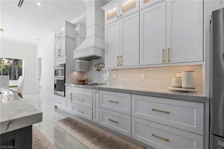 Kitchen with decorative backsplash, visible vents, marble finish floor, premium range hood, and appliances with stainless steel finishes