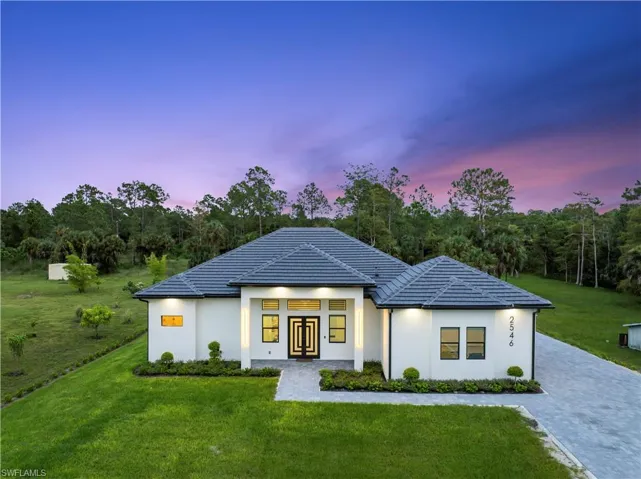 View of front facade featuring decorative driveway, a tile roof, stucco siding, french doors, and a yard