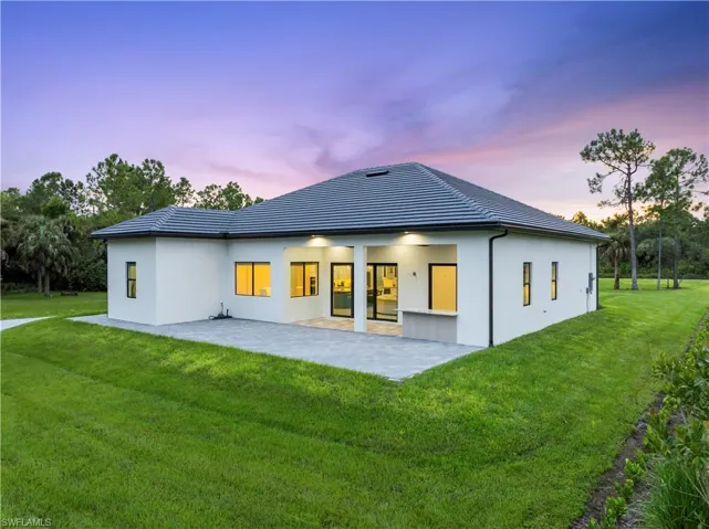 Back of property at dusk featuring a tiled roof, stucco siding, a patio, and a yard