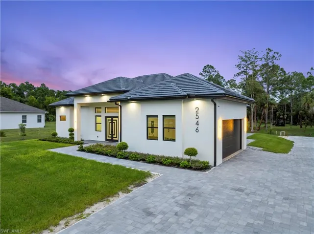 Prairie-style home with a tile roof, stucco siding, an attached garage, a lawn, and decorative driveway