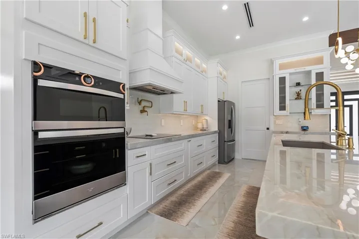 Kitchen with crown molding, marble finish floor, appliances with stainless steel finishes, a sink, and custom range hood