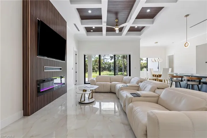 Living room featuring coffered ceiling, a glass covered fireplace, marble finish floor, baseboards, and a towering ceiling