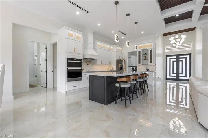 Kitchen featuring a large island with sink, a breakfast bar area, stainless steel double oven, marble finish floor, and custom range hood
