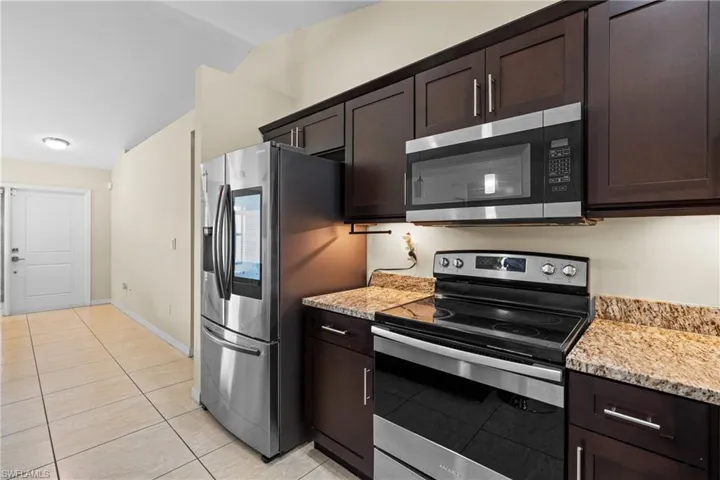 Kitchen featuring dark brown cabinetry, stainless steel appliances, light stone counters, and light tile patterned floors