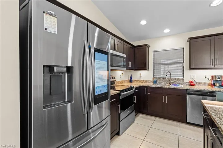 Kitchen with appliances with stainless steel finishes, dark brown cabinets, light tile patterned floors, light stone countertops, and vaulted ceiling