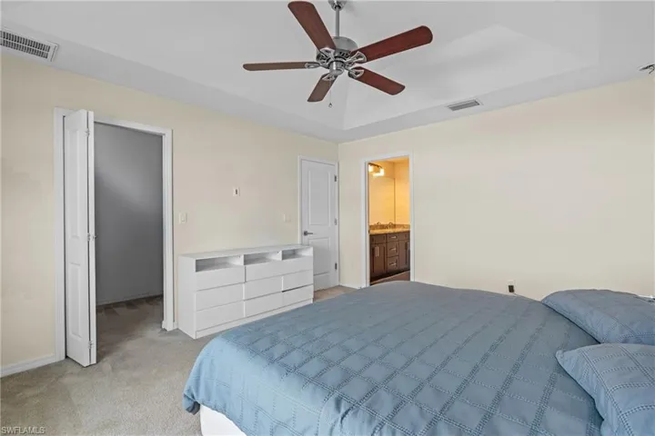 Bedroom featuring light carpet, a tray ceiling, and ceiling fan