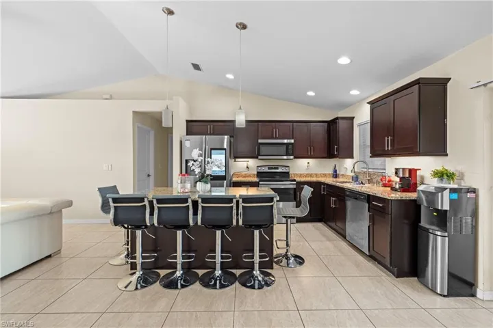 Kitchen with dark brown cabinets, decorative light fixtures, stainless steel appliances, a kitchen breakfast bar, and a center island