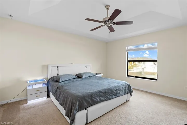 Carpeted bedroom featuring a ceiling fan and a raised ceiling