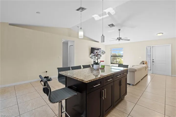 Kitchen with light stone countertops, decorative light fixtures, open floor plan, a kitchen island, and lofted ceiling