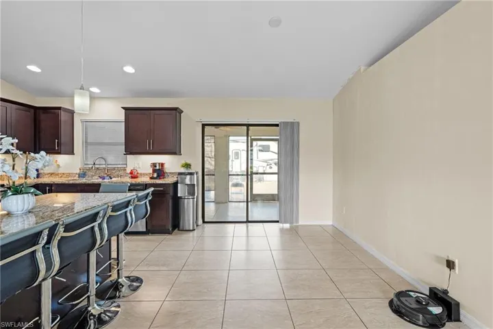 Kitchen with dark brown cabinetry, hanging light fixtures, light stone countertops, light tile patterned floors, and stainless steel dishwasher