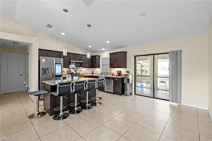 Kitchen with dark brown cabinets, a center island, a breakfast bar, hanging light fixtures, and light stone counters