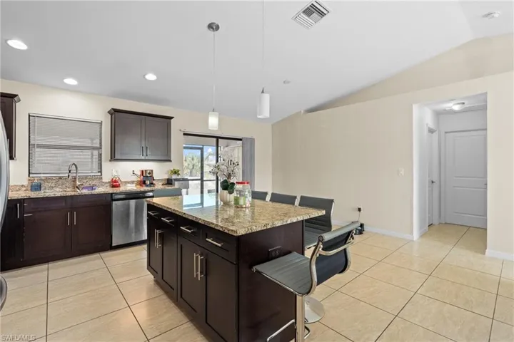 Kitchen featuring hanging light fixtures, dishwasher, light stone countertops, light tile patterned flooring, and dark brown cabinets