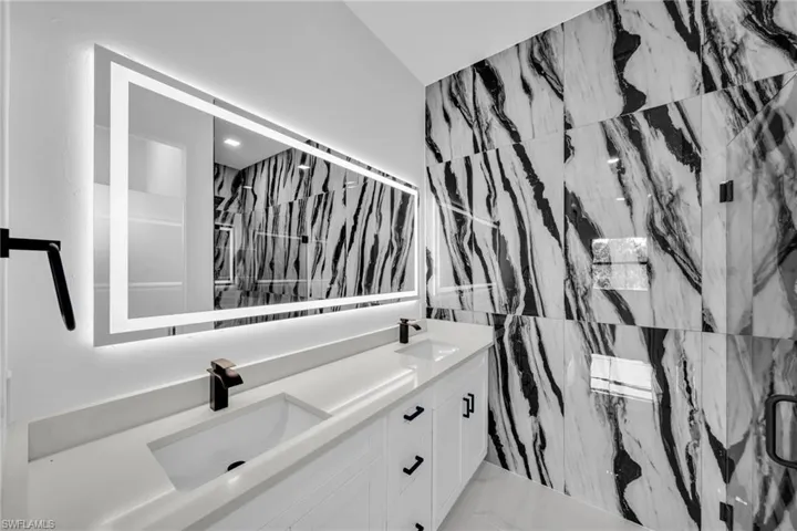 Full bath featuring double vanity, a marble finish shower, and marble finish floors