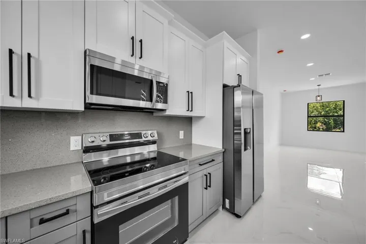 Kitchen with appliances with stainless steel finishes, light marble finish floors, light stone counters, recessed lighting, and white cabinets