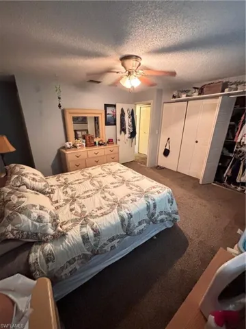 Bedroom with a textured ceiling, ceiling fan, a closet, and dark colored carpet