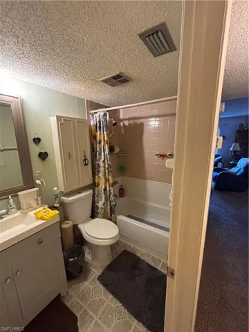 Bathroom featuring shower / bath combo, vanity, a textured ceiling, and light tile patterned flooring