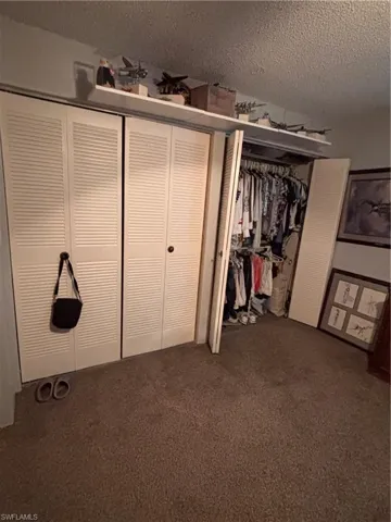 Unfurnished bedroom with a textured ceiling, dark colored carpet, and two closets