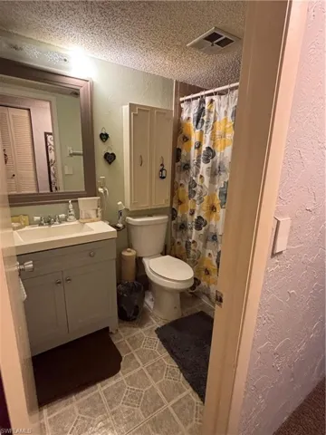 Bathroom with a textured wall, a shower with shower curtain, a textured ceiling, vanity, and light tile patterned floors