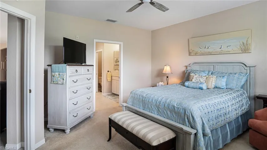 Carpeted master bedroom featuring ceiling fan and ensuite bath