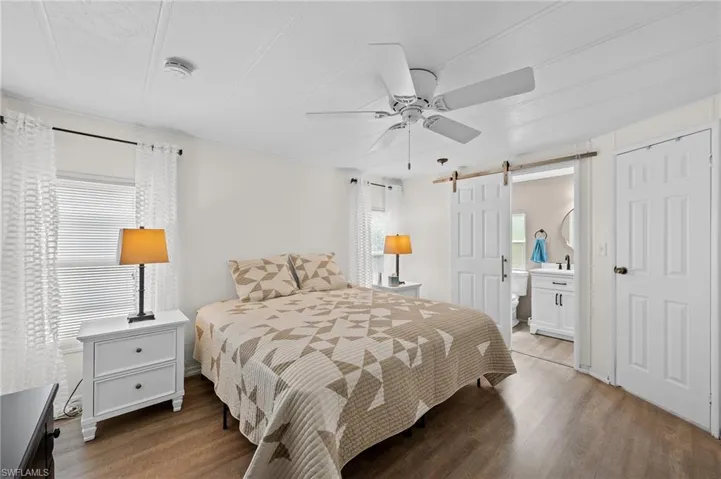 Bedroom featuring a barn door, ensuite bathroom, ceiling fan, and light wood finished floors