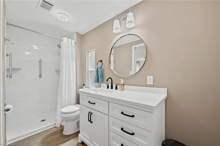 Full bath with a tile shower, vanity, visible vents, toilet, and wood finished floors