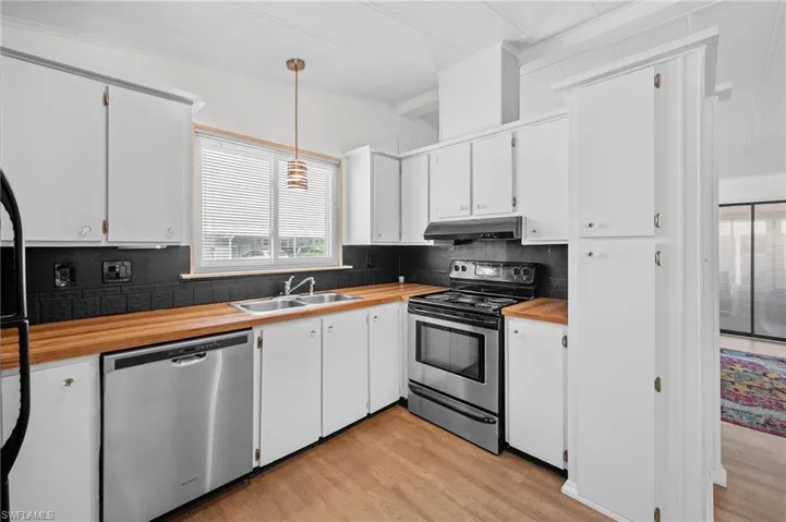 Kitchen with butcher block counters, appliances with stainless steel finishes, under cabinet range hood, a sink, and backsplash