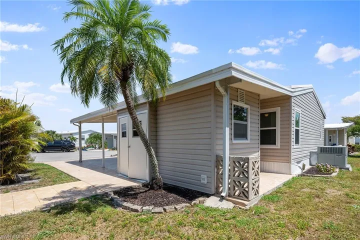 View of property exterior featuring a carport, cooling unit, and a lawn