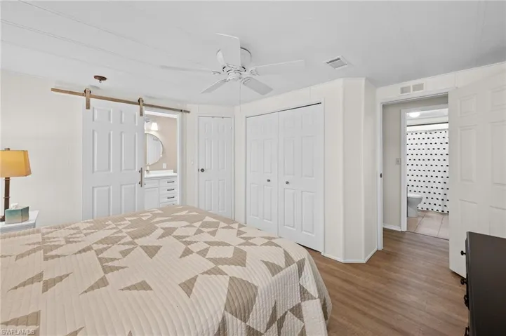 Bedroom with a barn door, visible vents, multiple closets, and wood finished floors