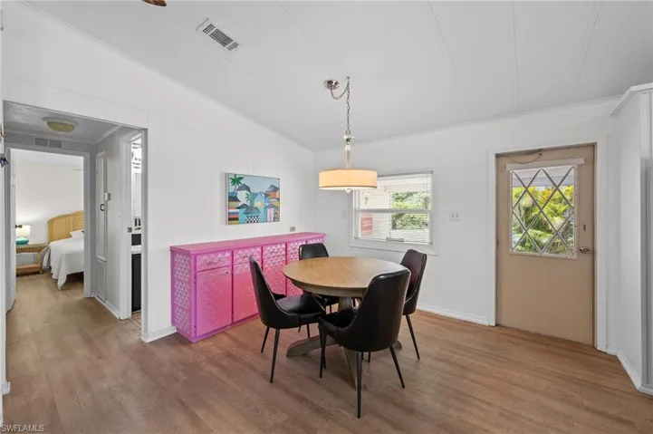 Dining room featuring ornamental molding, visible vents, wood finished floors, and vaulted ceiling