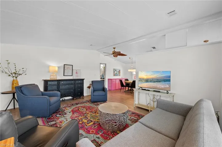 Living room featuring wood finished floors, ceiling fan, vaulted ceiling with beams, and visible vents
