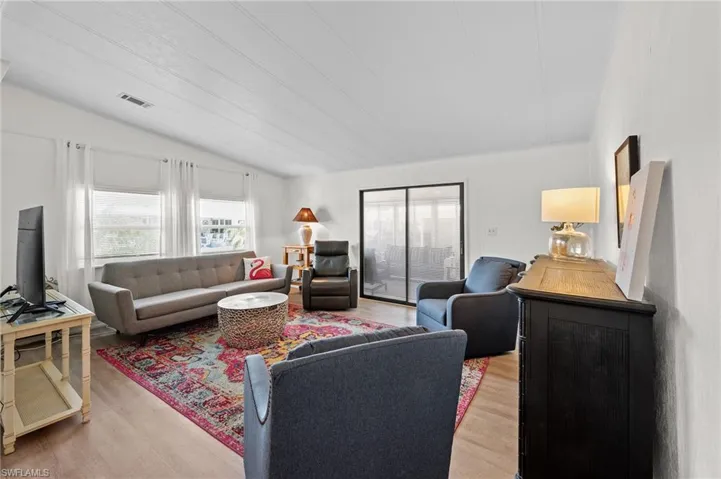 Living area with light wood-type flooring, visible vents, and lofted ceiling