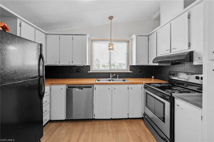 Kitchen with backsplash, under cabinet range hood, light wood-style floors, appliances with stainless steel finishes, and a sink
