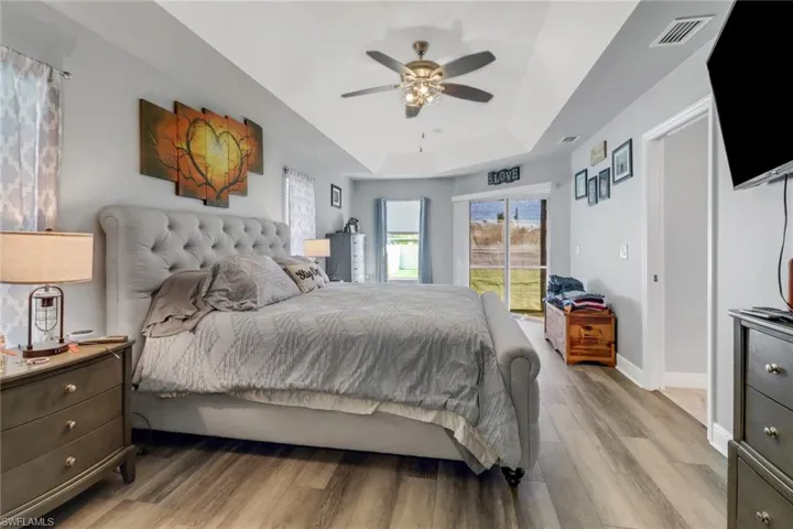 Bedroom with light hardwood / wood-style flooring, a raised ceiling, and ceiling fan