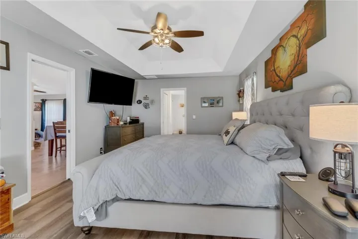 Bedroom featuring ceiling fan, a raised ceiling, and light wood-type flooring