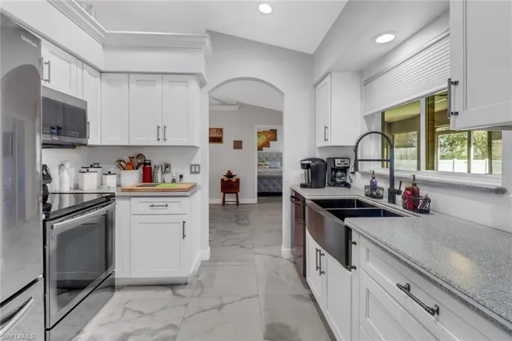 Kitchen with appliances with stainless steel finishes, sink, vaulted ceiling, white cabinets, and crown molding