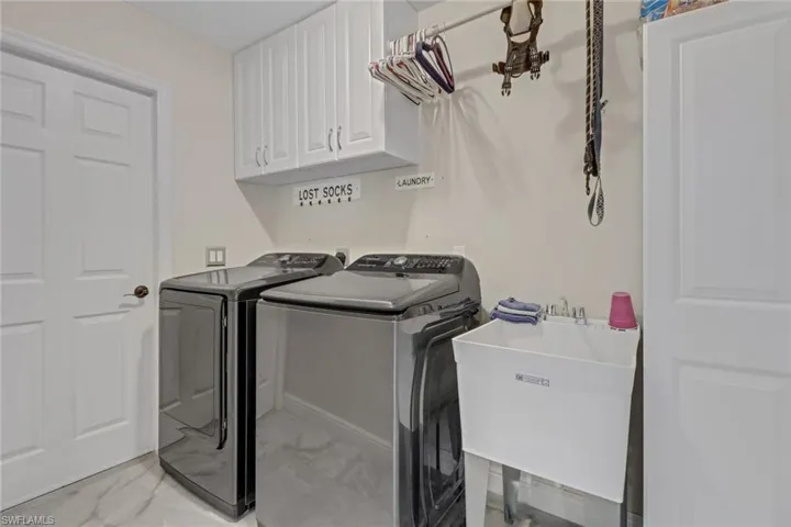 Clothes washing area featuring sink, washer and clothes dryer, and cabinets