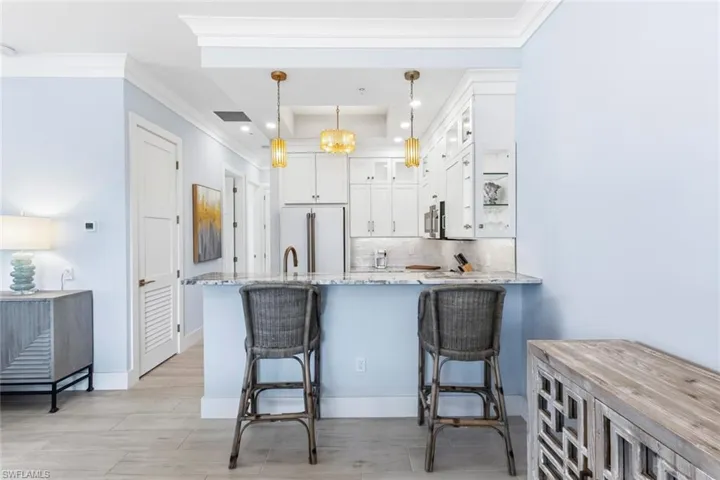 Kitchen featuring glass fronted cabinets, white cabinets, light stone countertops, pendant lighting, and a peninsula. Breakfast bar, Tray ceiling and accent lighting. GE Cafe Appliances. Range with Double Oven