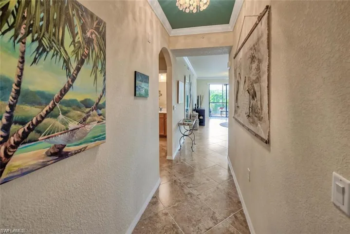 Hall featuring ornamental molding, a textured wall, arched walkways, and tile patterned flooring