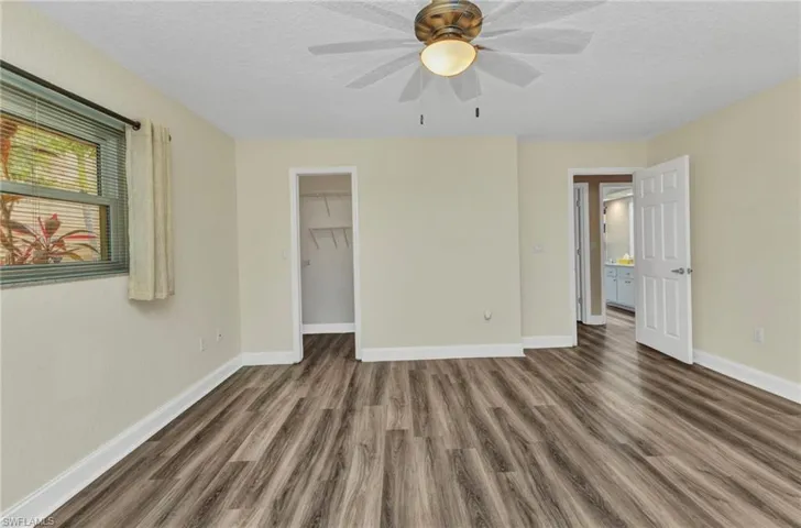 Unfurnished bedroom with baseboards, a textured ceiling, wood finished floors, and a spacious closet