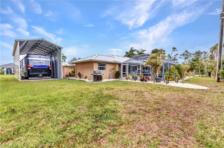 Back of property featuring glass enclosure, stucco siding, a carport, a patio area, and a lawn