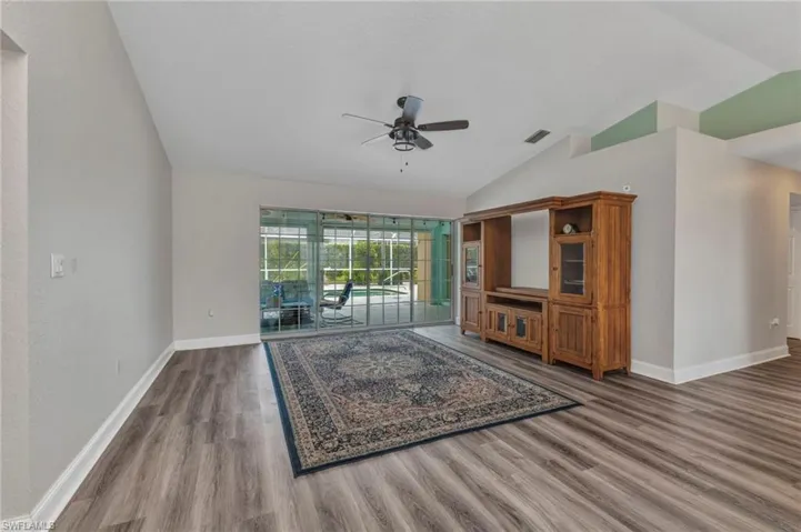 Unfurnished living room featuring a ceiling fan, wood finished floors, visible vents, baseboards, and lofted ceiling