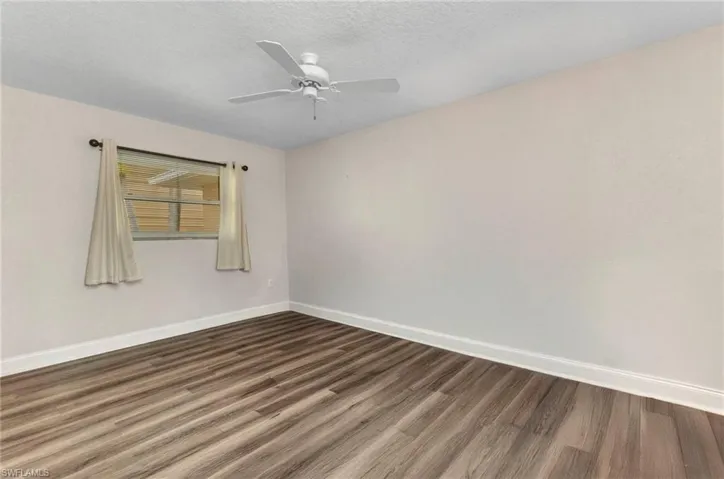 Empty room with ceiling fan, baseboards, a textured ceiling, and dark wood-style floors